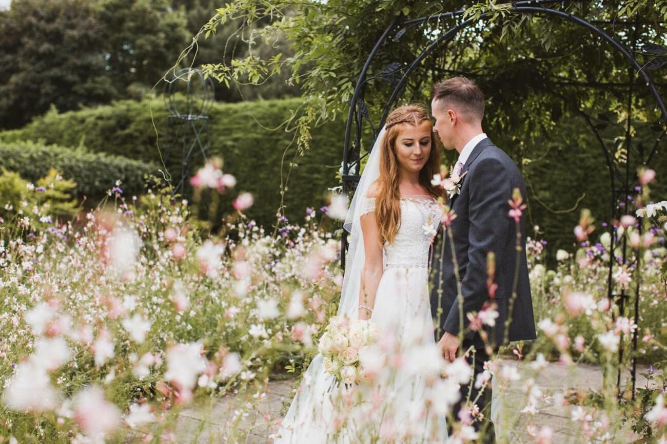 bride and groom in the walled garden at gaynes park surrounded by summer flowers