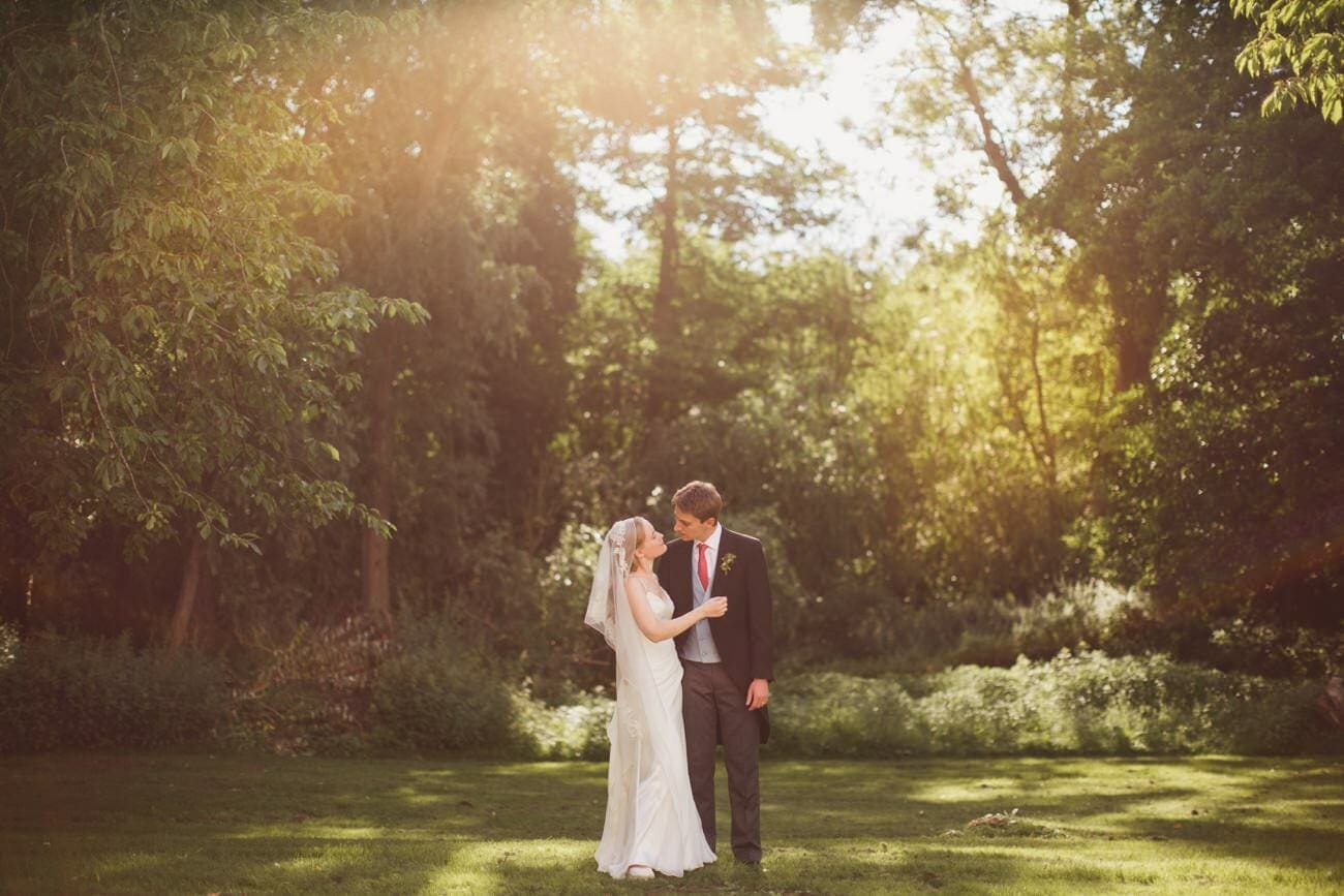 bride and groom in the grounds of butley priory looking at each other with the sun filtering through the trees
