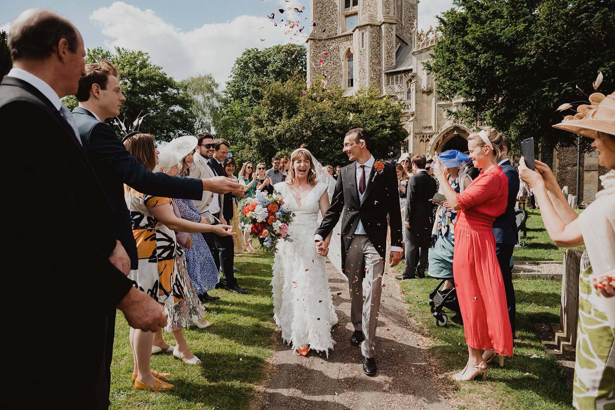 confetti being thrown outside suffolk church as bride and groom walk through it
