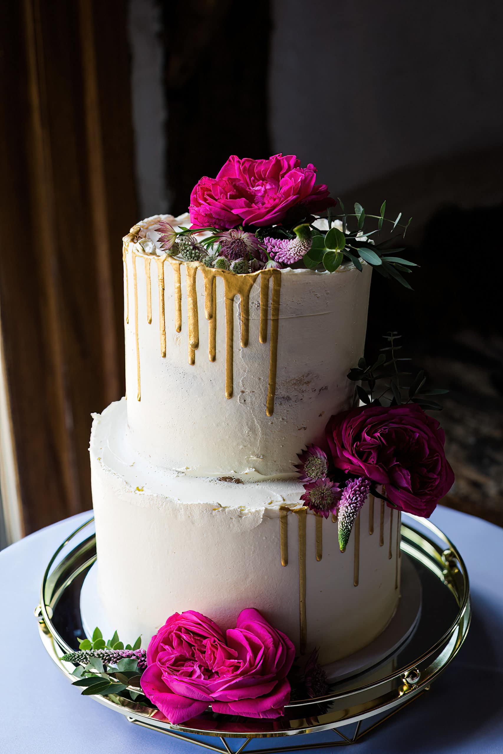 wedding cake with bright pink roses and a gold drip