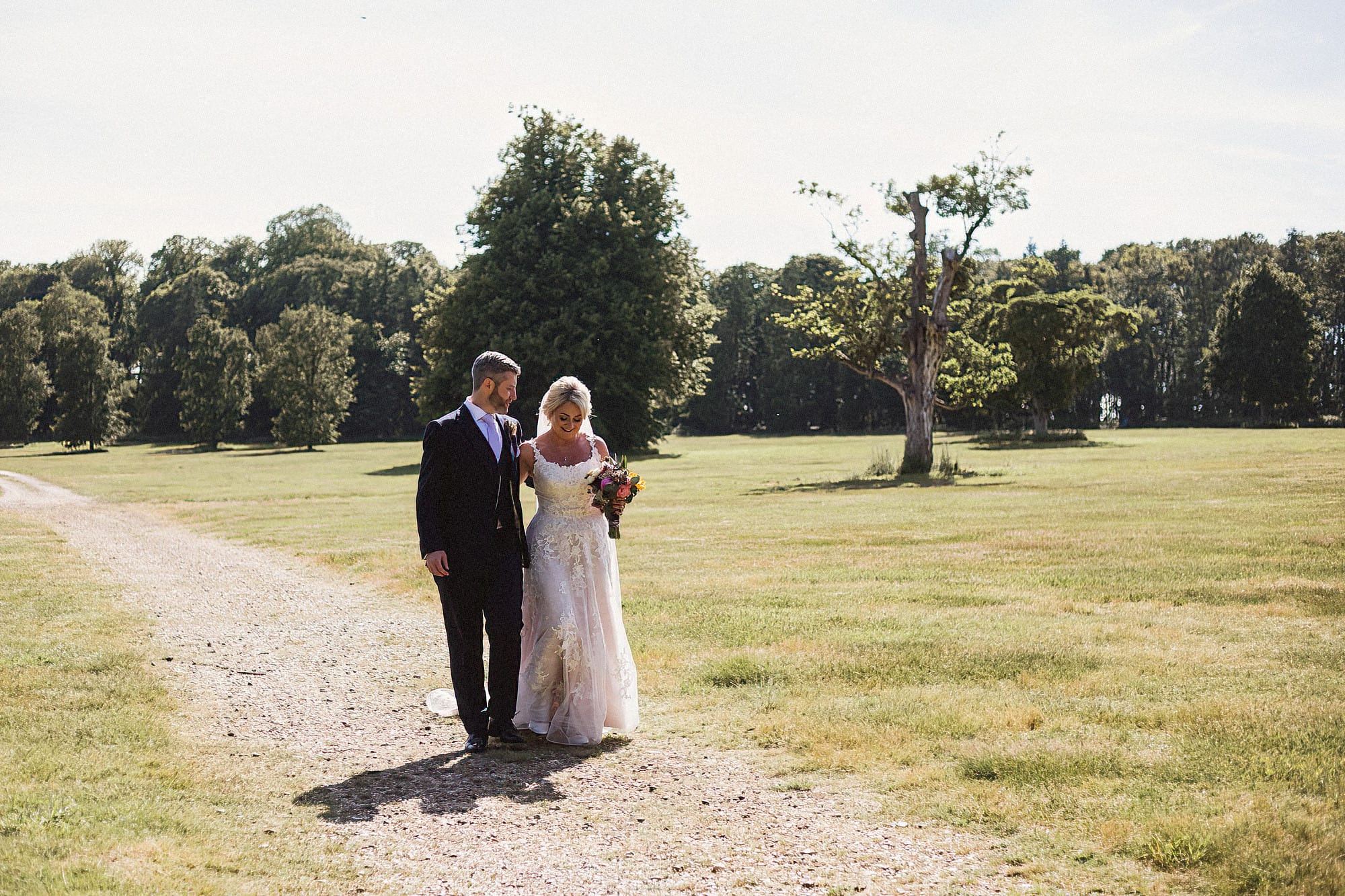 bride and groom walking through parkland at henham park