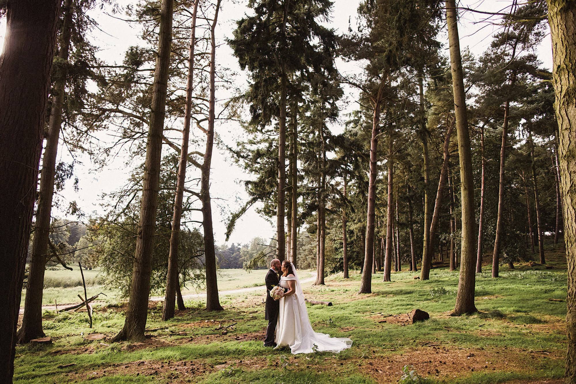 bride and groom walking through woodland at henham park