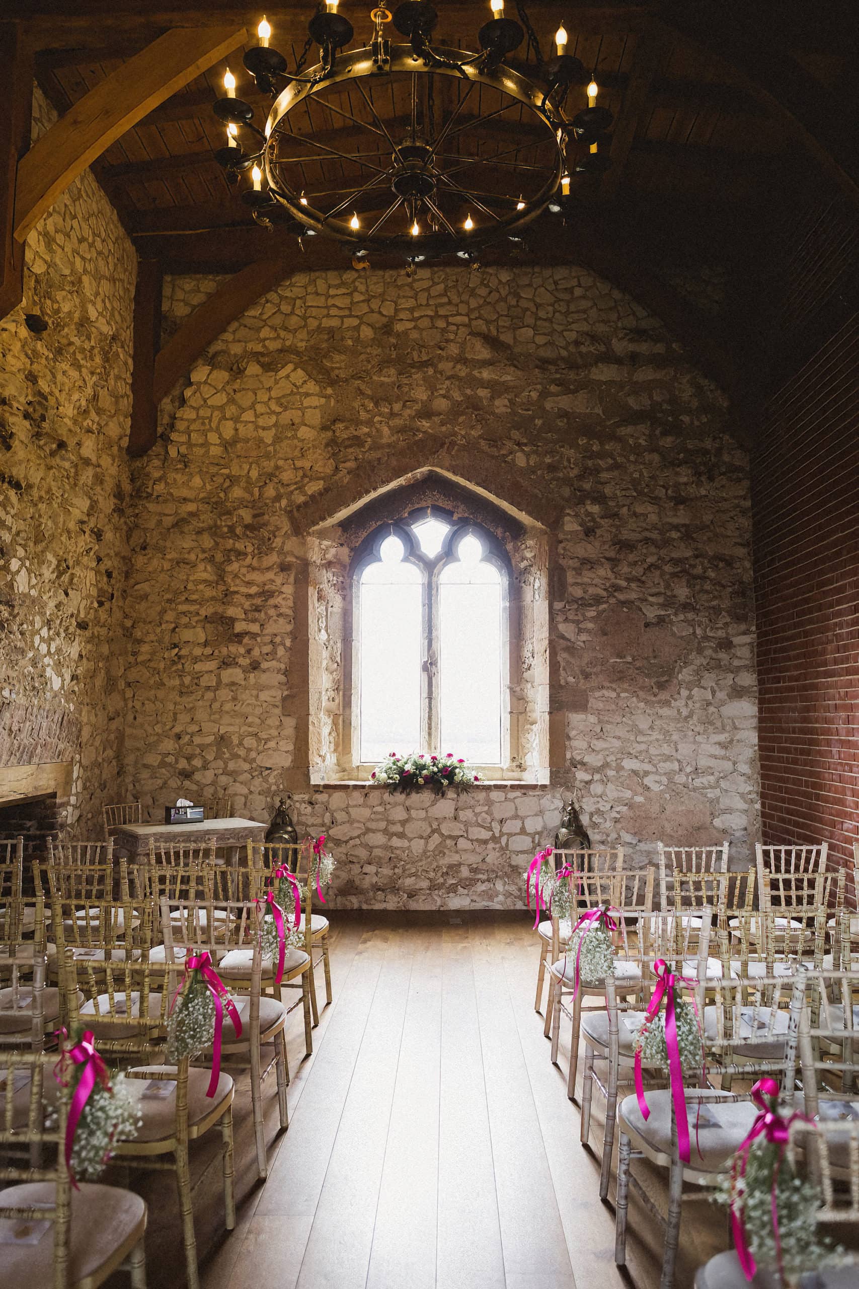 inside pentney abbey set up ready for a wedding ceremony. stone walls. white chairs. flowers lining the aisle