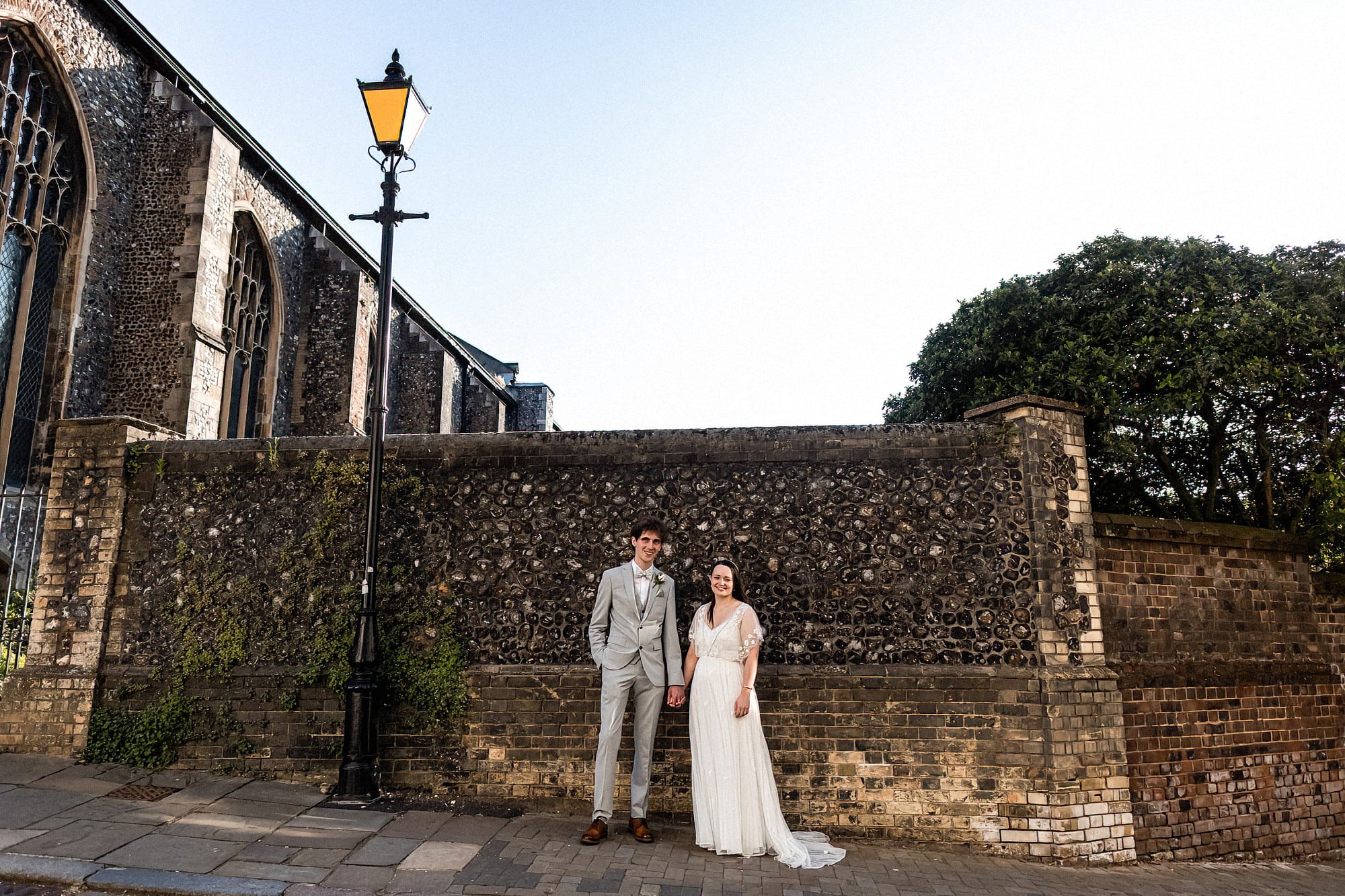 bride and groom standing posing for photo on elm hill norwich in front of old flint wall
