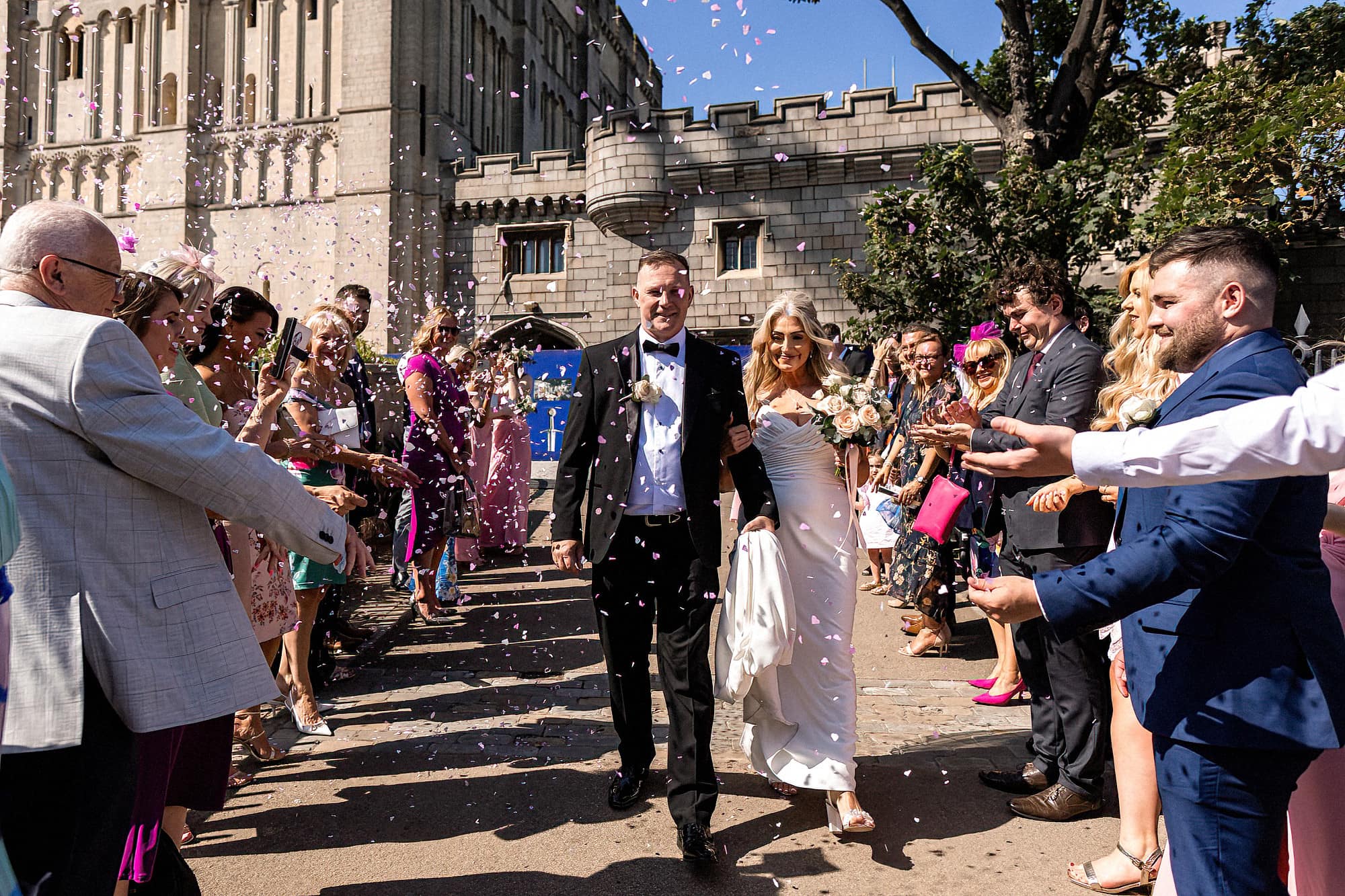 bride and groom walking through confetti at norwich castle on the bridge