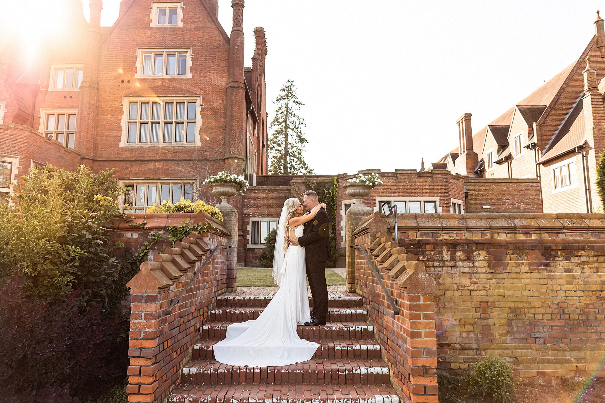 bride and groom standing posing on steps at dunston hall with the sun setting in the background
