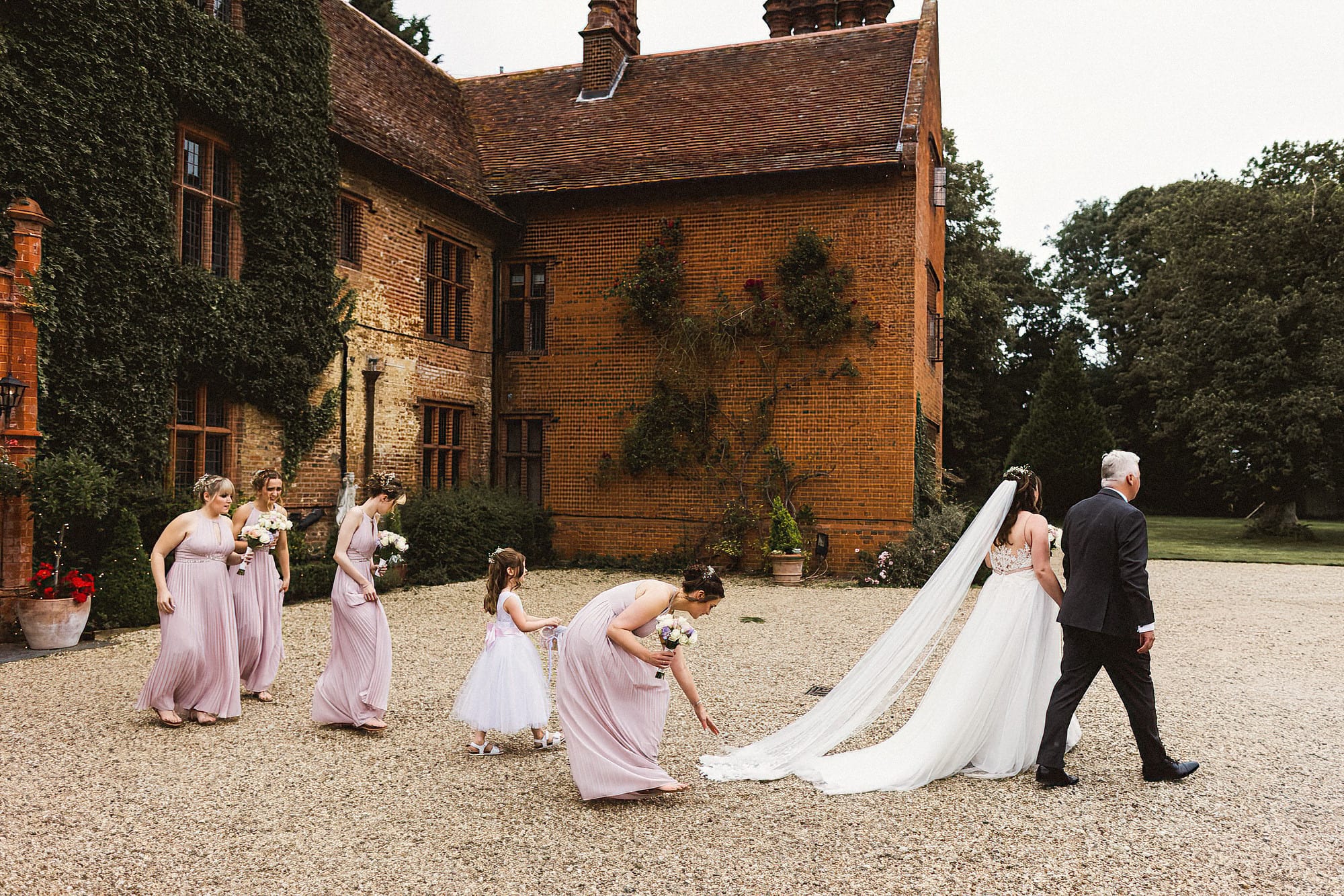 bride, dad and bridesmaids walking across the driveway of woodhall manor