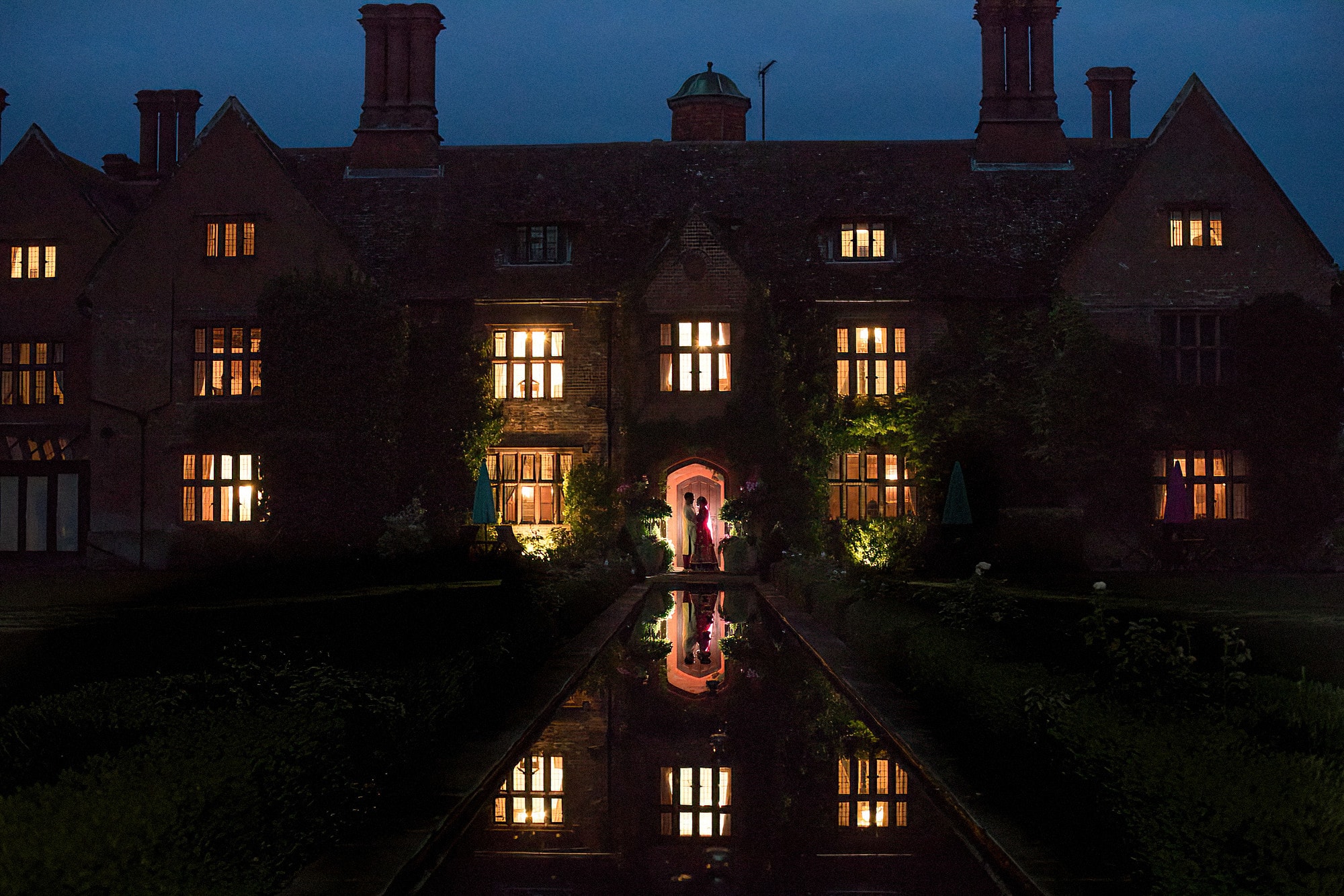woodhall manor at night with bride and groom backlit and reflection in pond