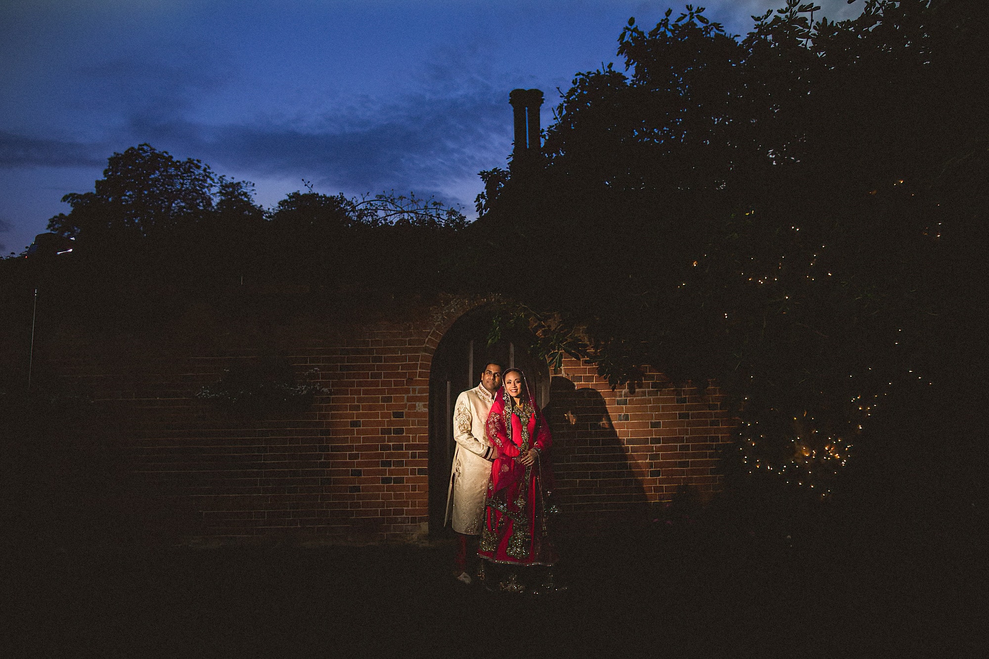 bride and groom at dusk standing in front of a wall and arched door