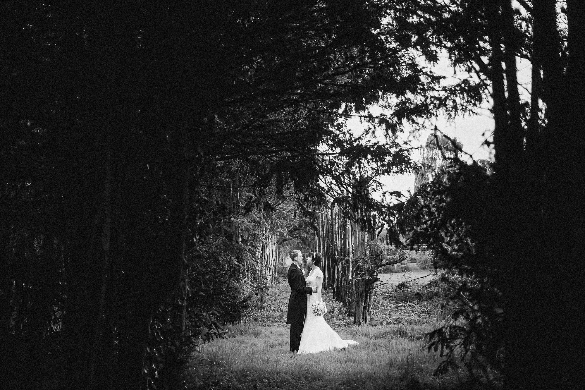 bride and groom standing for a photo in the woods facing each other