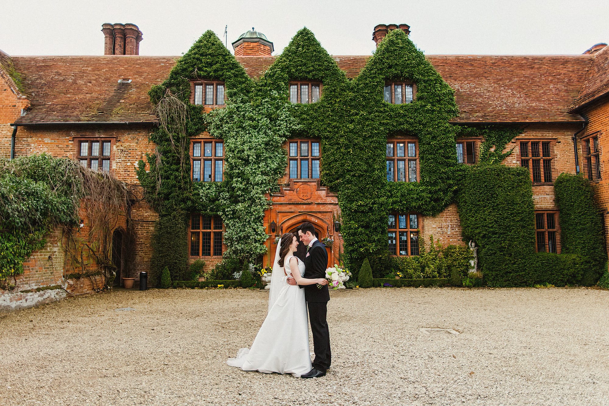 bride and groom standing in front of woodhall manor facing each other