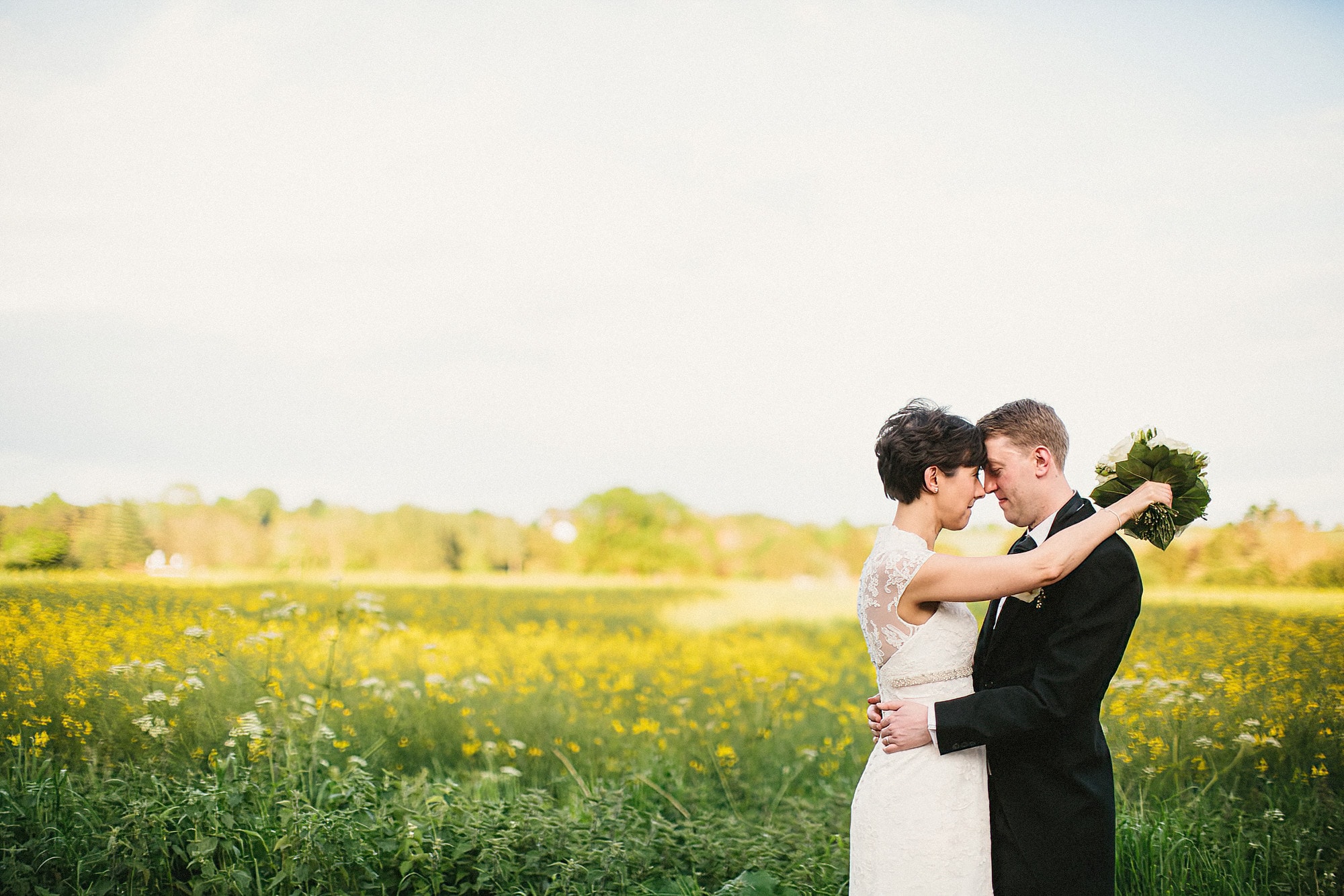 bride and groom standing in front of rape field facing each other and cuddling