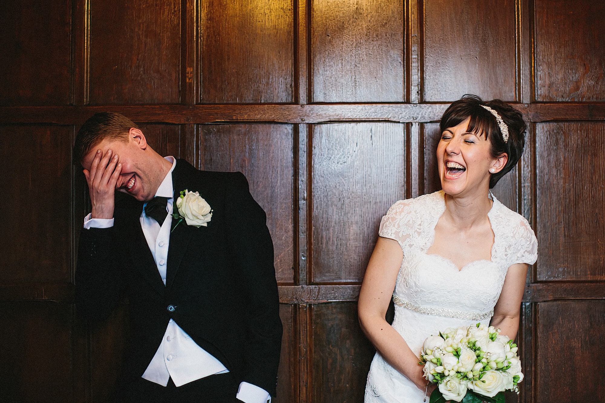 bride and groom laughing in front of dark wood panelling