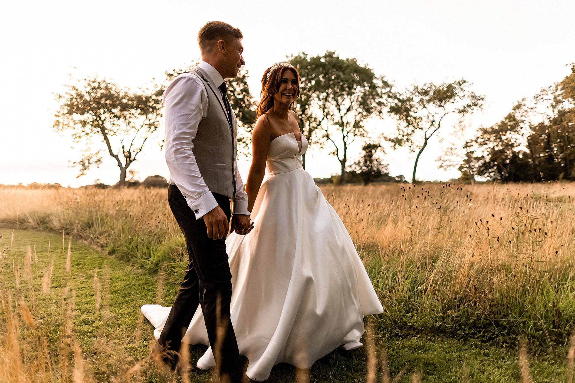 bride and groom walking hand in hand across the grounds at reymerston hall in golden hour